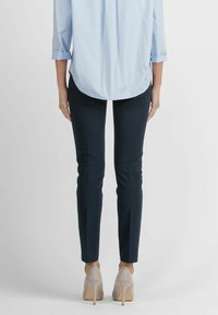 Marineblauwe slim-fit broek gemaakt van een gladde stof, gecombineerd met een lichtblauw overhemd met knopen. De hakken zijn lichtgrijs en hebben een spitse neus.