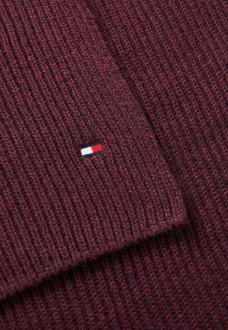 Burgundy ribbed knit fabric with a small embroidered logo in red, white, and blue on a corner. Soft texture with visible stitching patterns.