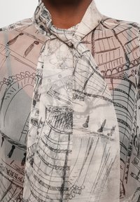 Durchsichtige Bluse mit großen abstrakten schwarz-weißen architektonischen Skizzen auf leichtem Stoff, locker mit einer Schleife am Hals gebunden.