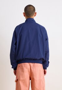 Marinblå bomberjacka med ribbat nederkant och ärmslut, med en slät yta och minimalistisk design, i kombination med rosa cargobyxor.