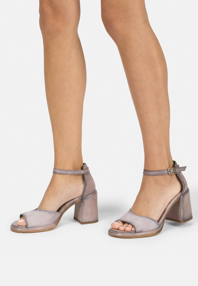 Open-toe block-heeled sandals in a soft, metallic lavender material with ankle strap and buckle detail. Smooth texture, minimalistic design.