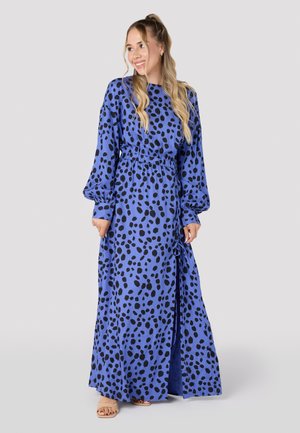 Maxi dress in blue fabric with black spot pattern, featuring long puff sleeves, an elastic waist, and a side slit for ease of movement.
