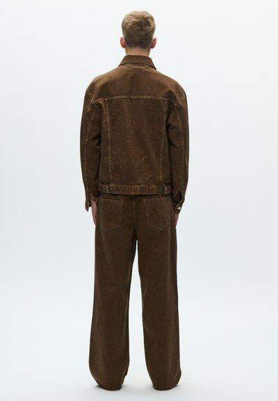 Jachetă din catifea cu dungi maro și pantaloni asortați, cu un croi lejer, detalii cu nasturi și o suprafață ușor texturată. Văzute din spate.