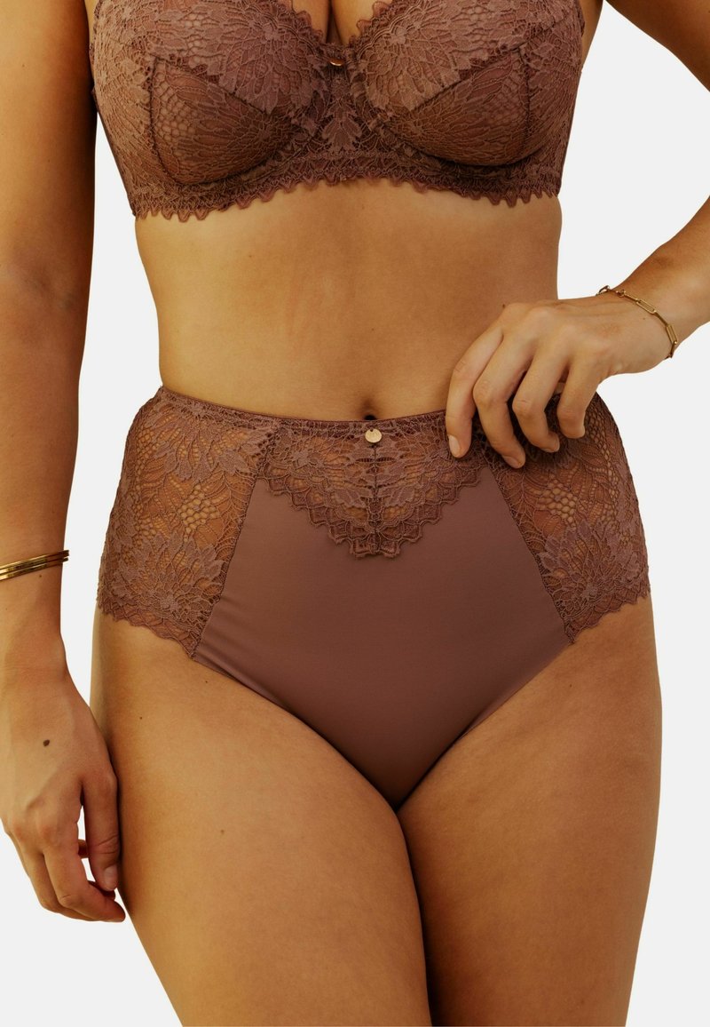 Culottes haute taille en dentelle brune avec une base en tissu lisse. Présentent des détails en dentelle complexes à la taille et un bouton décoratif à l'avant.