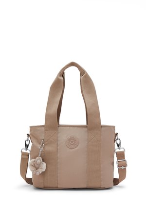 Beige fabric tote bag with wide handles, detachable shoulder strap, round brand logo, and plush monkey keychain on the side.