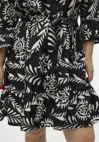 Vestido negro y blanco con estampado, con volantes y diseño floral, cinta de tela en la cintura y una textura suave.