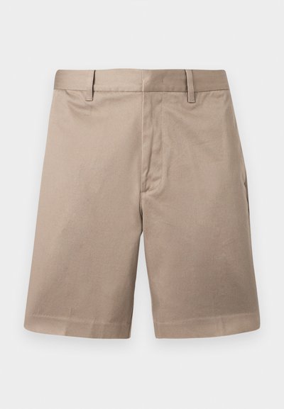 Μπεζ ελαφρώς μακρύ σόρτς chino με θηλιές για ζώνη, εμπρόσθιο ραφή και εφαρμοστή μέση, παρουσιασμένα σε απλό φόντο.