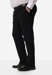 Pantaloni neri con una texture liscia, abbinati a scarpe nere. I pantaloni hanno un taglio dritto e sono indossati con una camicia bianca e una cintura nera.