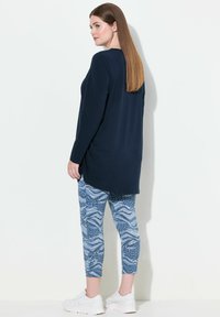 Maglietta a maniche lunghe blu navy con orlo arrotondato abbinata a leggins blu a motivi e sneakers bianche. Tessuto liscio con vestibilità rilassata.