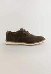 Zapato de ante marrón con cordones y acabado texturizado, suela en tono contraste marrón claro y detalles de costura sutiles. Punta redondeada y diseño de perfil bajo.