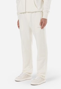 Pantalon de jogging en polaire blanche avec une taille �élastique, des poches latérales et un discret logo. Texture lisse, coupe décontractée et jambes droites.