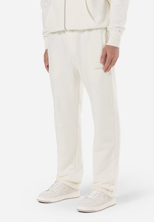 White fleece sweatpants with an elastic waistband, side pockets, and a subtle logo detail. Smooth texture, relaxed fit, and straight legs.