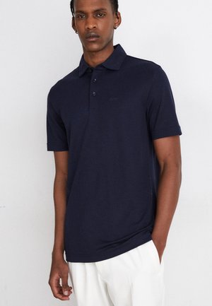 Polo shirt blu navy con colletto bottonato, maniche corte, in tessuto morbido, con un delicato dettaglio del logo sul petto. Texture liscia.