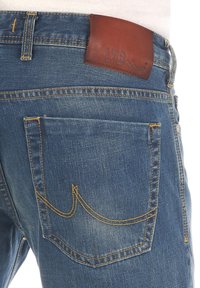 Mahones de mezclilla en azul con un acabado desgastado, con costuras amarillas y una etiqueta de cuero marrón en la cinturilla marcada "LTB". Diseño visible en el bolsillo trasero.