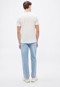 Λευκό κοντομάνικο μπλουζάκι, χαλαρή εφαρμογή, συνδυασμένο με ανοιχτό μπλε τζιν παντελόνι ίσιας γραμμής. Απλός σχεδιασμός με ομαλή υφή. Λευκά αθλητικά παπούτσια.