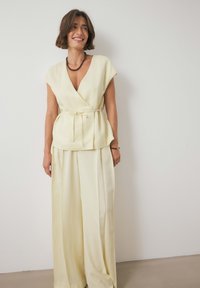 Gaiši dzeltens blūzes tops ar īsām piedurknēm, ar savilktu jostasvietu, apvienots ar vaļīgām, plašām biksēm. Gluda auduma ar subtilu spīdumu.