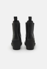 Bottines en cuir noir avec des panneaux élastiques sur les côtés, bout arrondi et talon épais. Texture lisse avec des détails de surpiqûres contrastées.