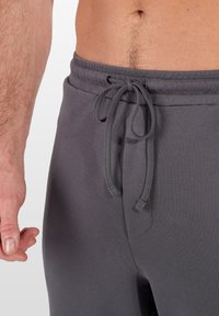Graue Sweatpants aus weichem Stoff mit einem elastischen Bund und Kordelzug. Verfügt über eine Seitentasche und eine glatte, gleichmäßige Oberfläche.