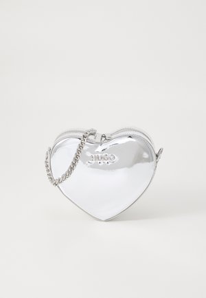 Silberne, herzförmige Tasche mit glänzender Oberfläche, Reißverschluss und silbernem Kettenriemen. Mit erhabenem "HUGO"-Logo auf der Vorderseite.