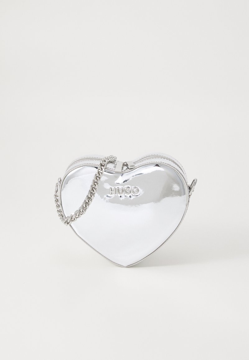 Borsa a forma di cuore argento con finitura lucida, chiusura con zip e tracolla in catena argentata. Presenta il marchio "HUGO" in rilievo sul davanti.