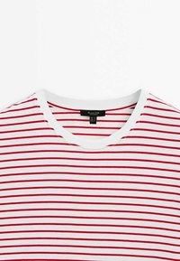 T-shirt rayé rouge et blanc avec un col rond, en tissu doux, présentant une étiquette au centre près du col.