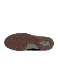 Semelle de sneaker noire et grise avec un dessous en caoutchouc brun texturé, affichant un motif de grip circulaire et le logo de la marque. Design durable et flexible.