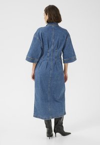 Denimkleit, mille on kitsendatud vöökoht, kolmandiku pikkuses varrukad ja pikk hem. Omab kontrastseid õmblusi ja struktureeritud kaelust.