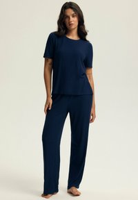 Granatowy komplet piżamowy z prążkowanej tkaniny, składający się z bluzki z krótkim rękawem i okrągłym dekoltem oraz luźnych spodni. Miękka faktura, swobodny krój.