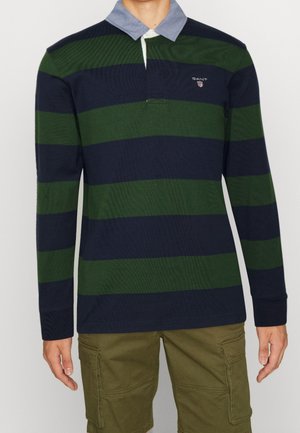 Polo à manches longues rayé bleu marine et vert, avec un col bleu clair et un détail de logo. Associé à un short cargo beige.