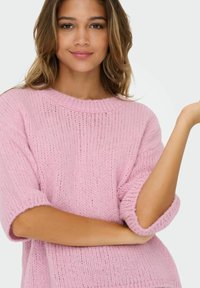 Roze gebreide trui met een ronde hals en korte opgerolde mouwen. De stof lijkt zacht en heeft een textuur, met een loose fit.