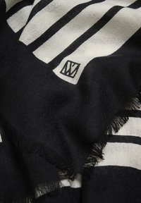 Mustvalge triibuline kangas, mille äärtes on lahtised kiud ja millel on väike kangast silt, kus on stiliseeritud "W" logo.