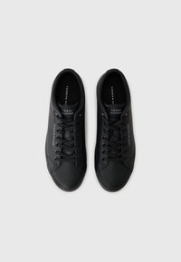 Zapatillas de cuero negro con textura suave, puntera redonda, diseño de cordones y marca en la lengüeta. Estilo minimalista con un brillo sutil.