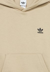 Μπεζ βαμβακερό φούτερ με κουκούλα, που διαθέτει μπροστινή τσέπη, ριμπ μανσέτες και μι�κρό μαύρο λογότυπο adidas στο αριστερό στήθος. Μαλακή υφή, casual σχεδιασμός.