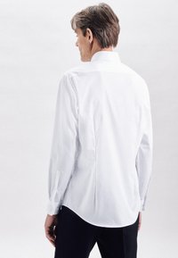 Witte lange mouwen shirt met een achterpand, knoopmanchetten en een afgeronde zoom, gemaakt van een gladde stof. Draagt bij donkere broek.