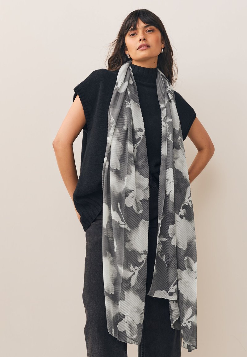 Musta hihaton neulepaita, harmaa kukkakuvioinen huivi ja tummat housut. Huivi on kuvioitu raidoin ja pehmein kukkasin, ja siinä on teksturoitu ulkonäkö.