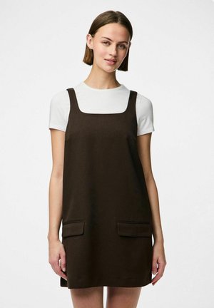 Mörkbrun A-linjeformad klänning med fyrkantig halsringning, två framfickor och något strukturerad tyg, lager på en vit t-shirt.