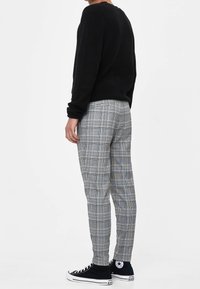 Černý pletený svetr, šedé kostkované kalhoty s modrými akcenty, přiléhavý střih a černé plátěné tenisky. Viditelné detaily v barvách a textuře.