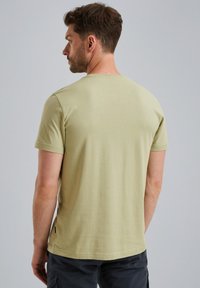 Jasnooliwkowy t-shirt z krótkim rękawem, okrągłym dekoltem i gładką fakturą. Posiada subtelną metkę marki na dolnej krawędzi.