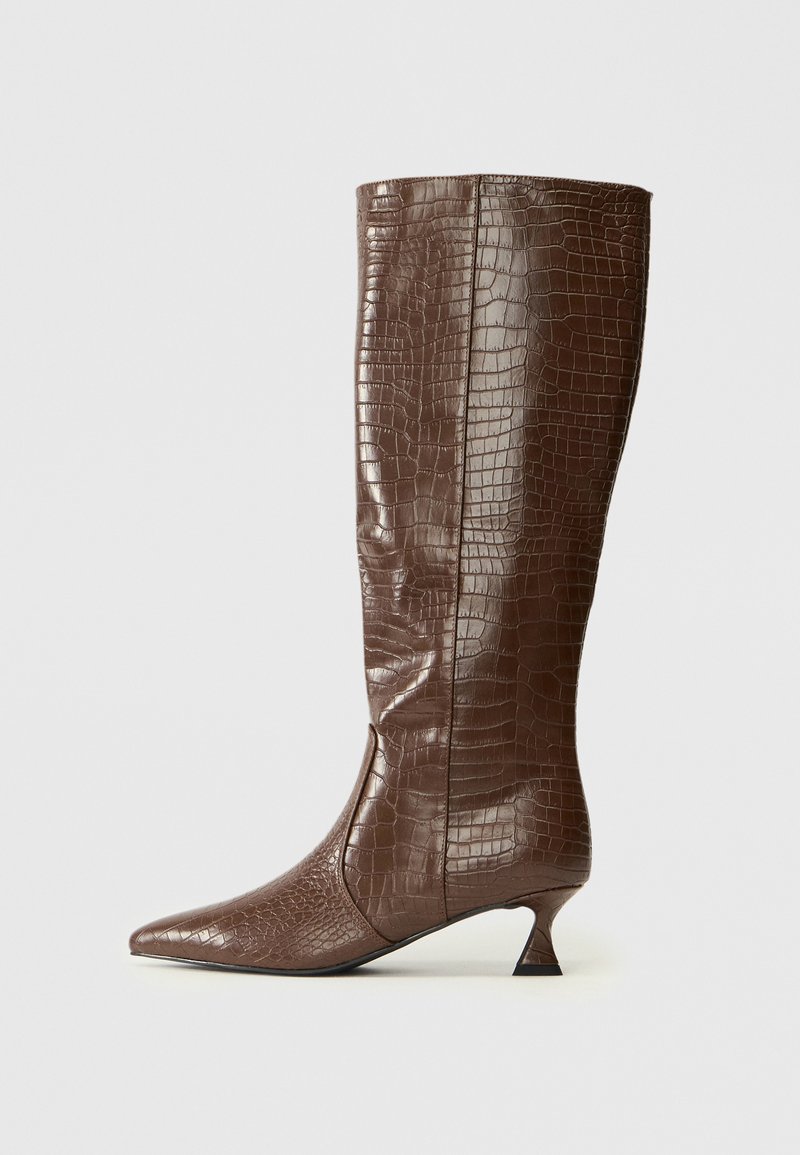 Bottes marron jusqu'au genou en matière imitant le crocodile. Bout pointu et talons fins, texture lisse, design élégant avec une silhouette ajustée.