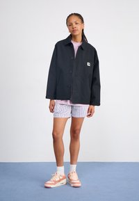 Zwarte overhemdjasje, gestreepte shorts en perzikkleurige sneakers met witte accenten. Soepele stof, relaxte pasvorm en detail van een borstzak aan de voorkant.