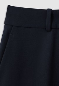 Prim-plan al taliei pantalonilor din țesătură bleumarin închis, cu buclă pentru curea și țesătură subtil texturată.