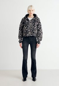 Skraćena jakna s leopard uzorkom od mekog materijala, sa kapuljačom i prednjim zatvaračem, u kombinaciji s tamnim trapezasto krojenim trapericama i crnim čizmama na špic.