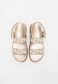 DKNY sandaler har en metallisk gullfarge på overdelen med to trykte stoffstropper og en justerbar ankelrem. Teksturert såle for grep.