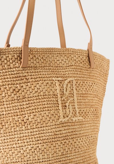 Sac cabas en paille tissée avec des poignées en cuir marron clair et un motif monogramme tressé sur le devant.