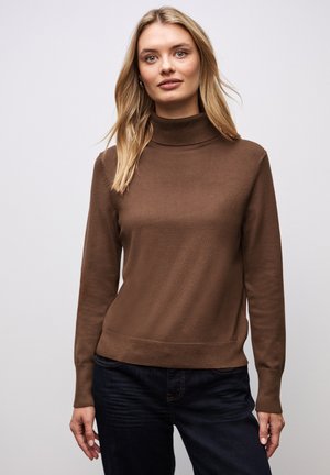 Brauner Rollkragenpullover aus weichem Stoff, mit taillierter Passform, langen Ärmeln und geripptem Saum. Kombiniert mit dunklen Jeans.