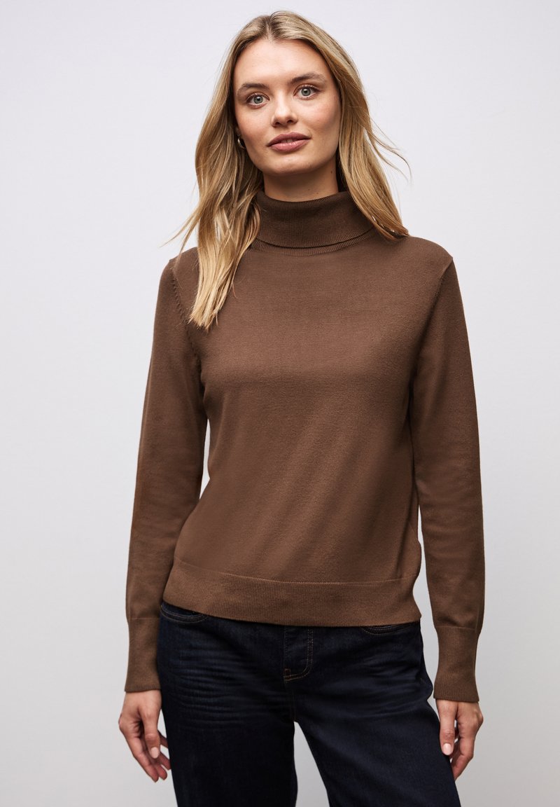 Brauner Rollkragenpullover aus weichem Stoff, mit taillierter Passform, langen Ärmeln und geripptem Saum. Kombiniert mit dunklen Jeans.