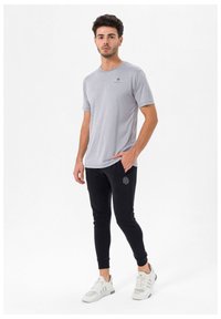 Grå T-shirt med korte ærmer og rund hals samt et lille sort logo, parret med sorte joggerbukser med et diskret logo og elastiske manchetter.