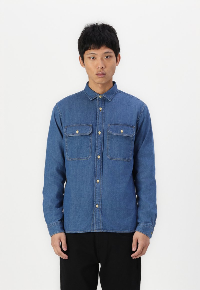 Denim button-up shirt in medium blue, features two chest pockets, gold buttons, and long sleeves with cuff buttons. Smooth texture.