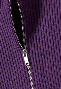 Tissu violet côtelé avec un détail de fermeture éclair argentée sur un côté, mettant en valeur une surface texturée. La fermeture éclair est partiellement ouverte.