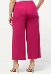 Pantaloni a gamba larga in fucsia vivace. Realizzati in tessuto strutturato, presentano una vita elasticizzata. Si indossano sandali con tacco trasparente.